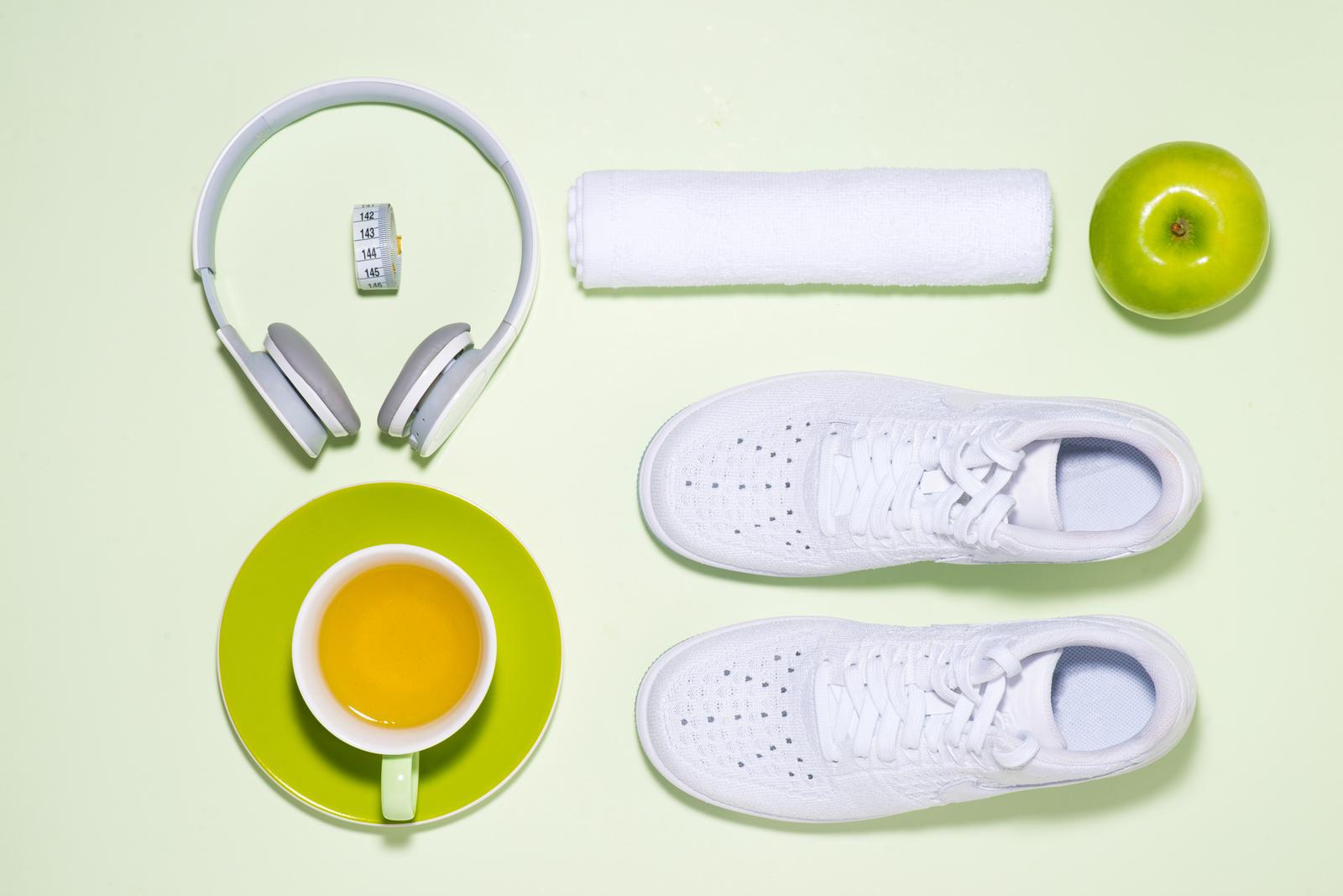 Fitness plan concept. Sneakers, tea, apple and headphone on pastel color background with open notebook.